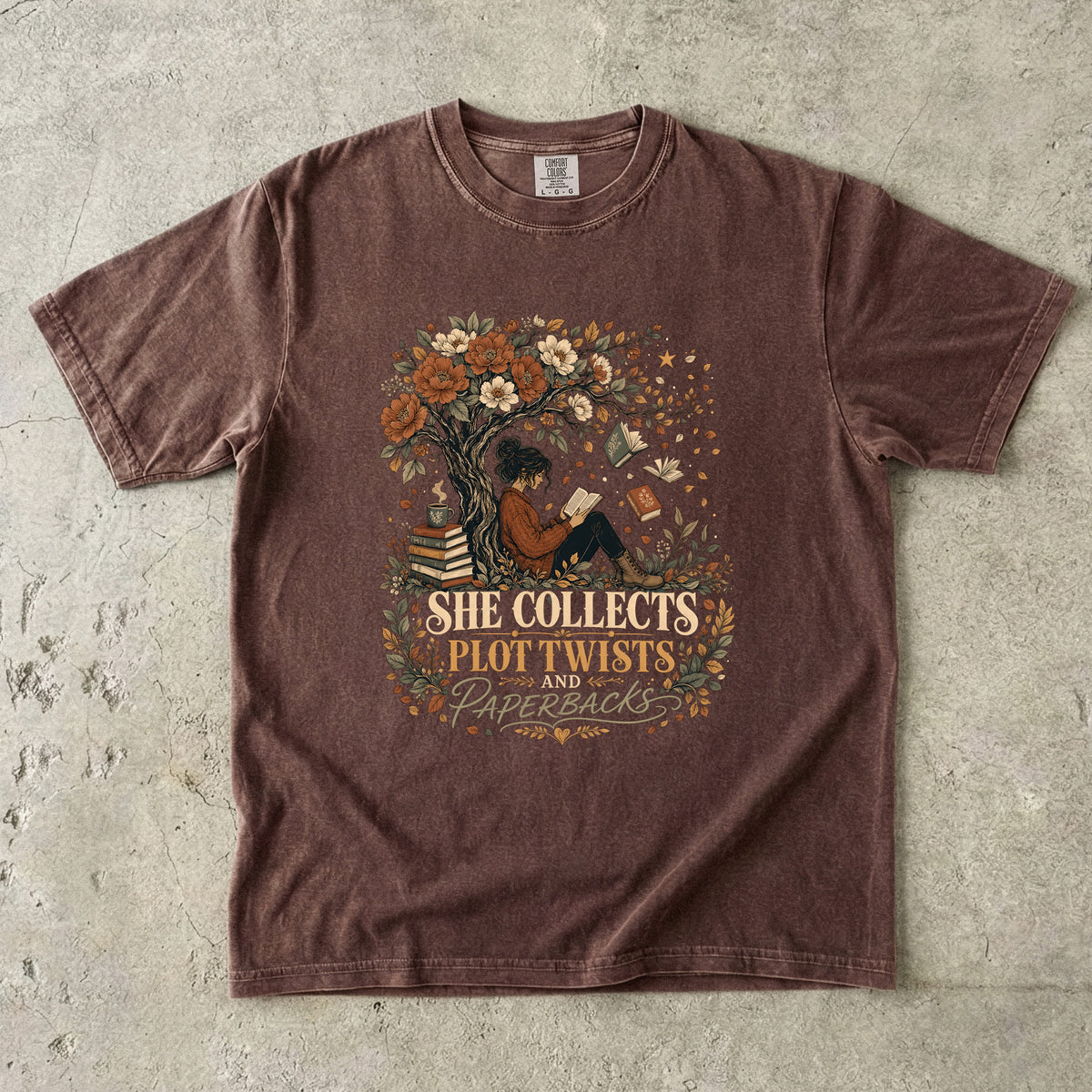 Espresso reading T-shirt featuring She Collects Plot Twists and Paperbacks with a reader beneath a flowering tree surrounded by books.