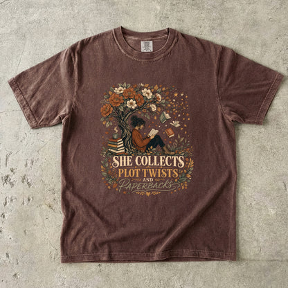 Espresso reading T-shirt featuring She Collects Plot Twists and Paperbacks with a reader beneath a flowering tree surrounded by books.