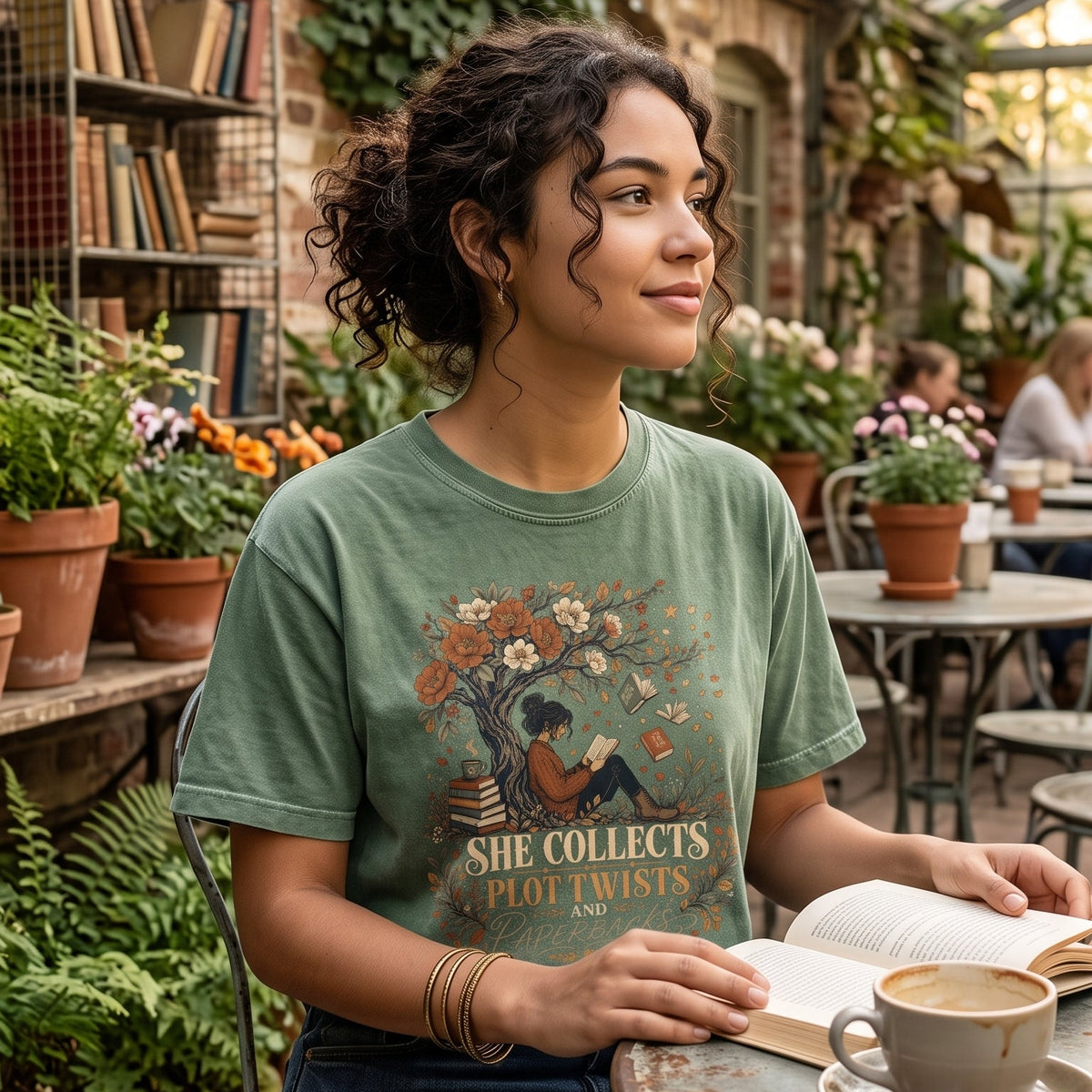She Collects Plot Twists and Paperbacks reading T-shirt featuring a reader beneath a flowering tree surrounded by books and leaves.