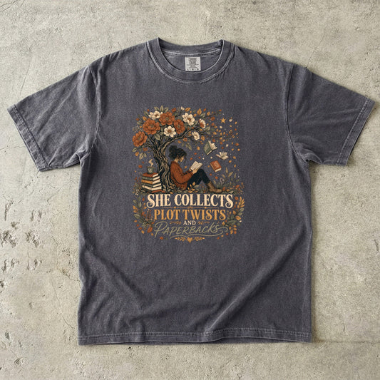 Pepper reading T-shirt featuring She Collects Plot Twists and Paperbacks with a reader beneath a flowering tree surrounded by books.