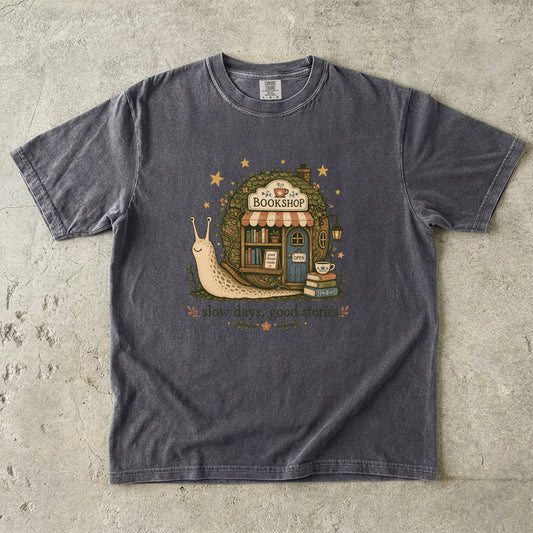 Slow Days, Good Stories Book Lover Shirt printed on a Pepper Comfort Colors 1717 T-shirt featuring a whimsical snail bookshop illustration.

