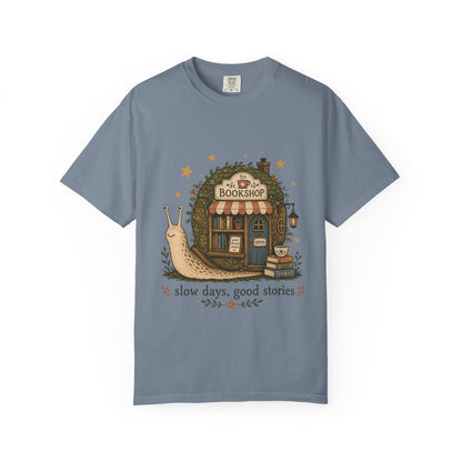 Slow Days, Good Stories bookshop T-shirt in Blue Jean featuring a snail beside a tiny bookshop with books and tea