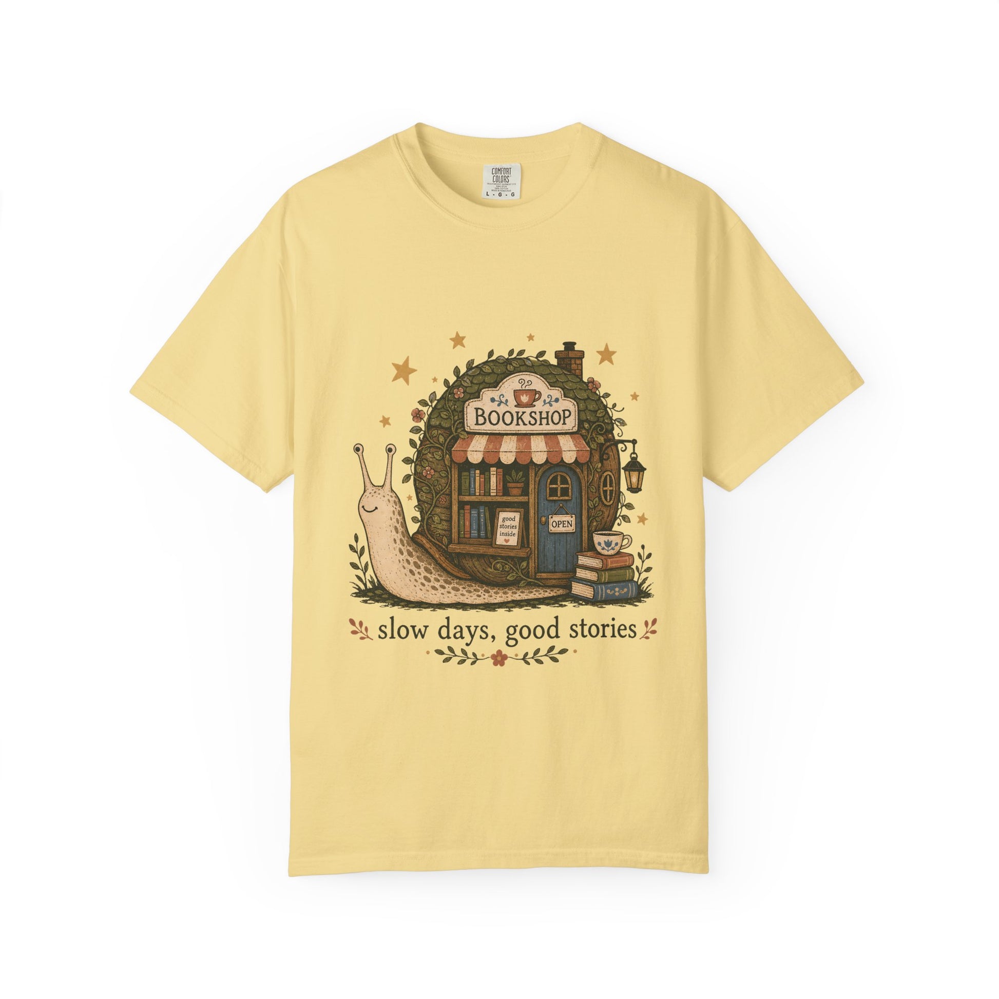 Slow Days, Good Stories bookshop T-shirt in Butter featuring a snail beside a tiny bookshop with books and tea