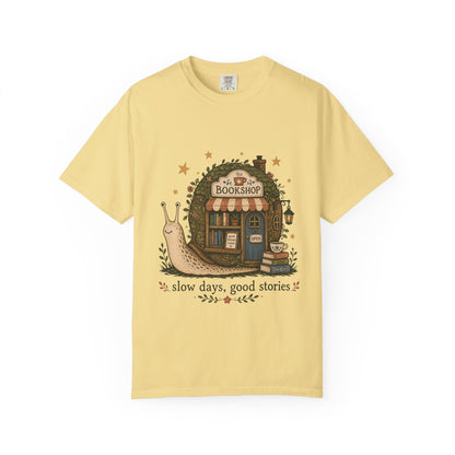 Slow Days, Good Stories bookshop T-shirt in Butter featuring a snail beside a tiny bookshop with books and tea