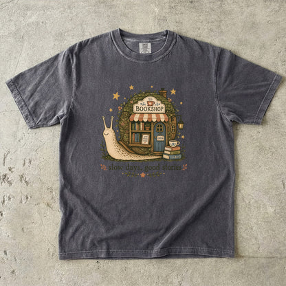 Slow Days, Good Stories bookshop T-shirt in Pepper featuring a snail beside a tiny bookshop with books and tea