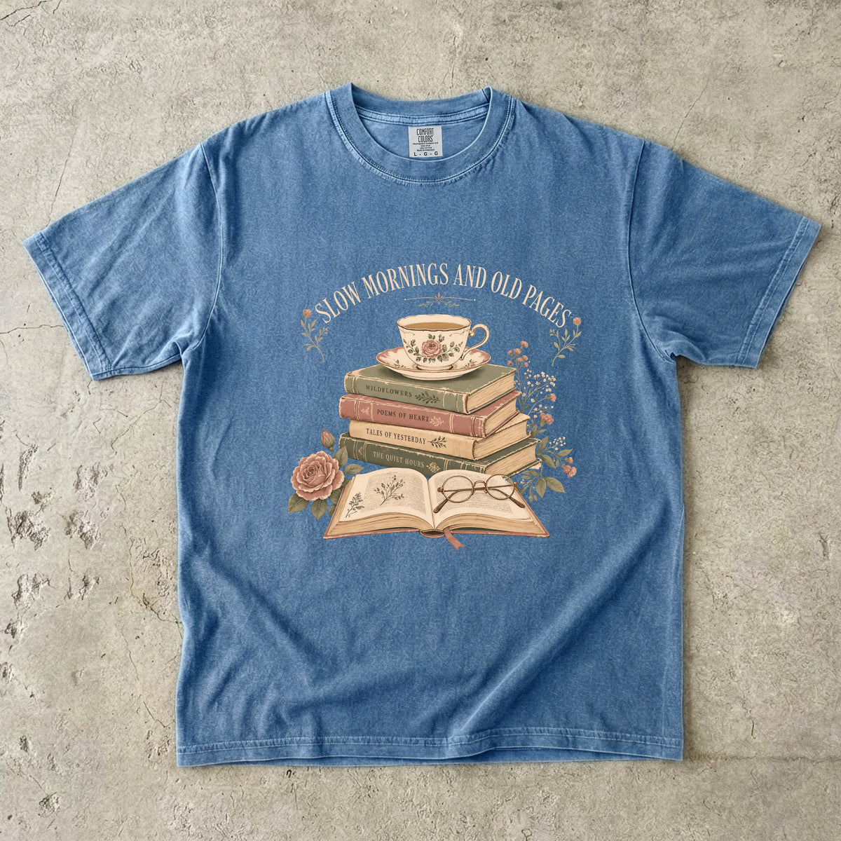 Blue Jean reading T-shirt featuring Slow Mornings and Old Pages with stacked vintage books, a floral teacup, open book, glasses and roses.