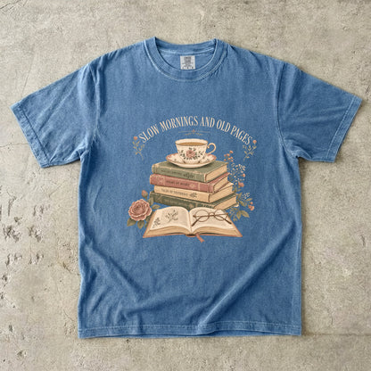 Blue Jean reading T-shirt featuring Slow Mornings and Old Pages with stacked vintage books, a floral teacup, open book, glasses and roses.