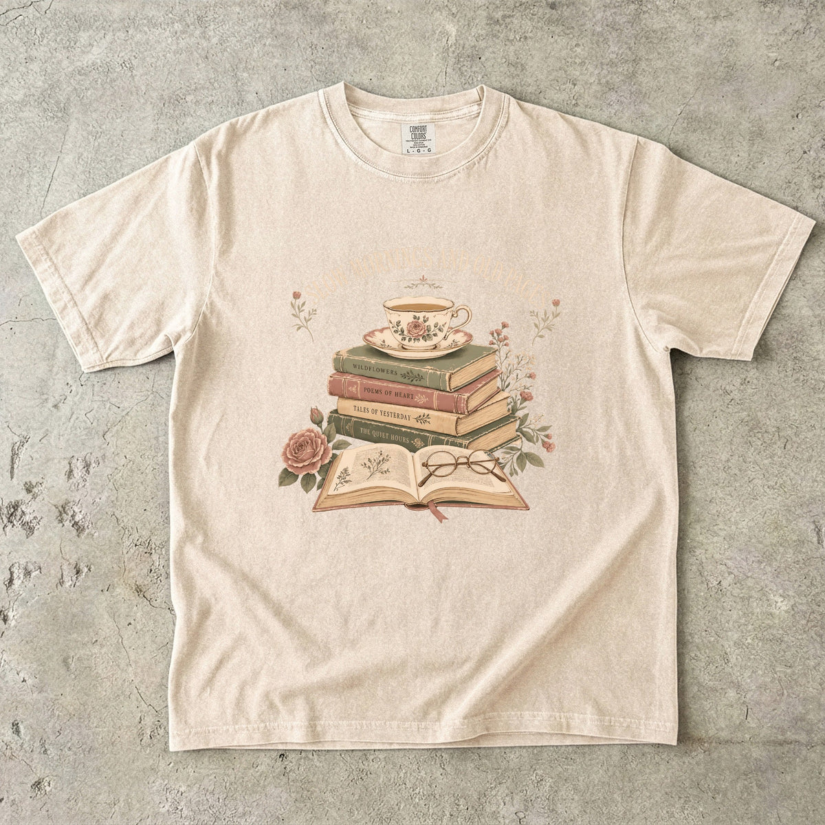 Ivory reading T-shirt featuring Slow Mornings and Old Pages with stacked vintage books, a floral teacup, open book, glasses and roses.