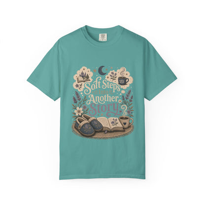 Soft Steps Into Another Story book lover shirt on a Comfort Colors seafoam T-shirt featuring vintage-inspired artwork with books, cosy slippers, flowers and coffee mugs.

