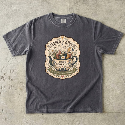 Steeped in Stories book lover T-shirt with a floral teapot overflowing with books on Pepper.