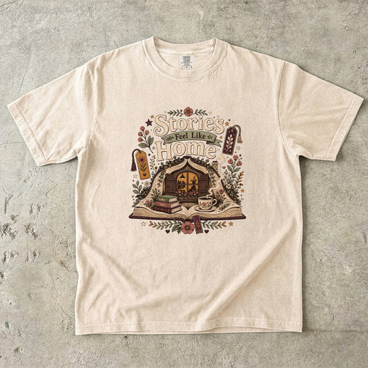 Stories Feel Like Home book lover T-shirt with open book, cozy reading nook, stacked books, teacup and floral details on Ivory.