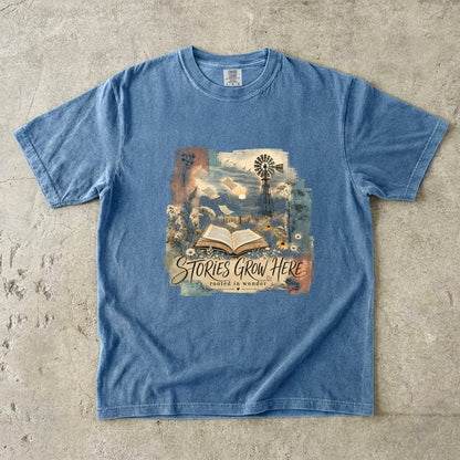 Blue Jean Comfort Colors Stories Grow Here book lover T-shirt featuring an open book, wildflowers and country landscape.