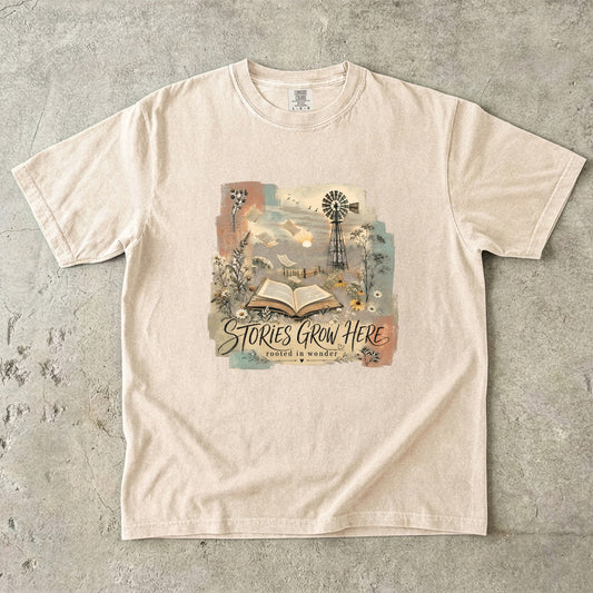 Ivory Comfort Colors Stories Grow Here T-shirt with an open book, wildflowers, windmill and dreamy landscape.