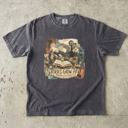 Pepper Comfort Colors Stories Grow Here reading T-shirt with an open book, wildflowers and countryside artwork.