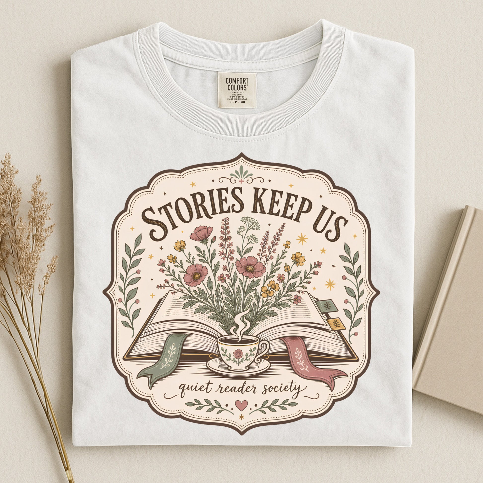 Folded white book lover T-shirt showing the Stories Keep Us vintage reading illustration.