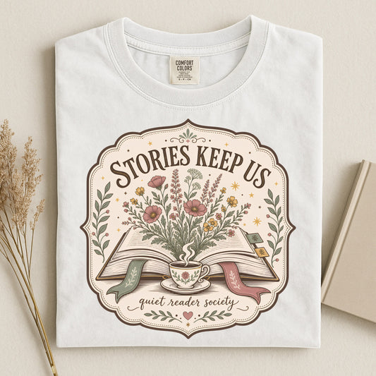 Folded white book lover T-shirt showing the Stories Keep Us vintage reading illustration.