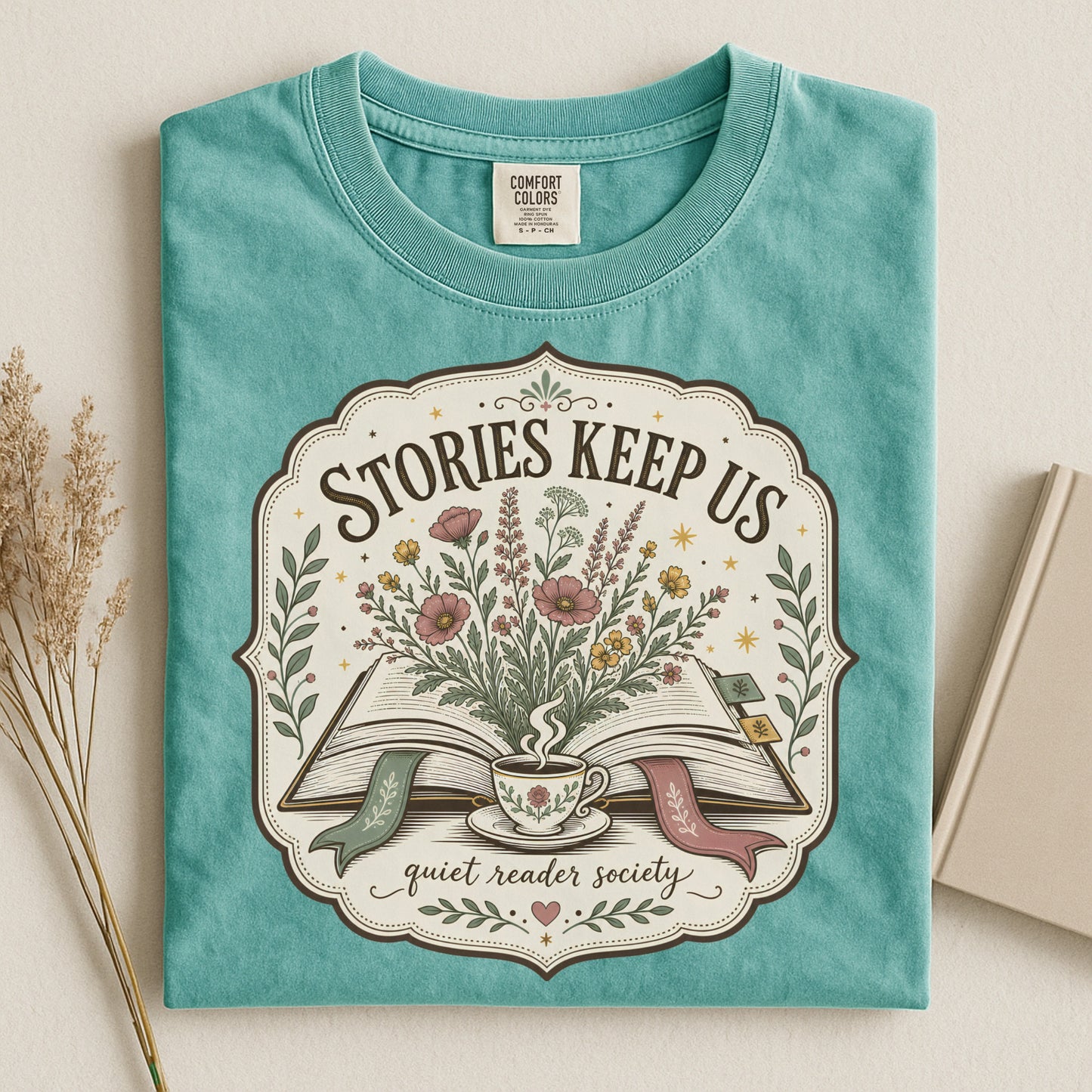 Folded seafoam Stories Keep Us book-inspired T-shirt with floral literary artwork.