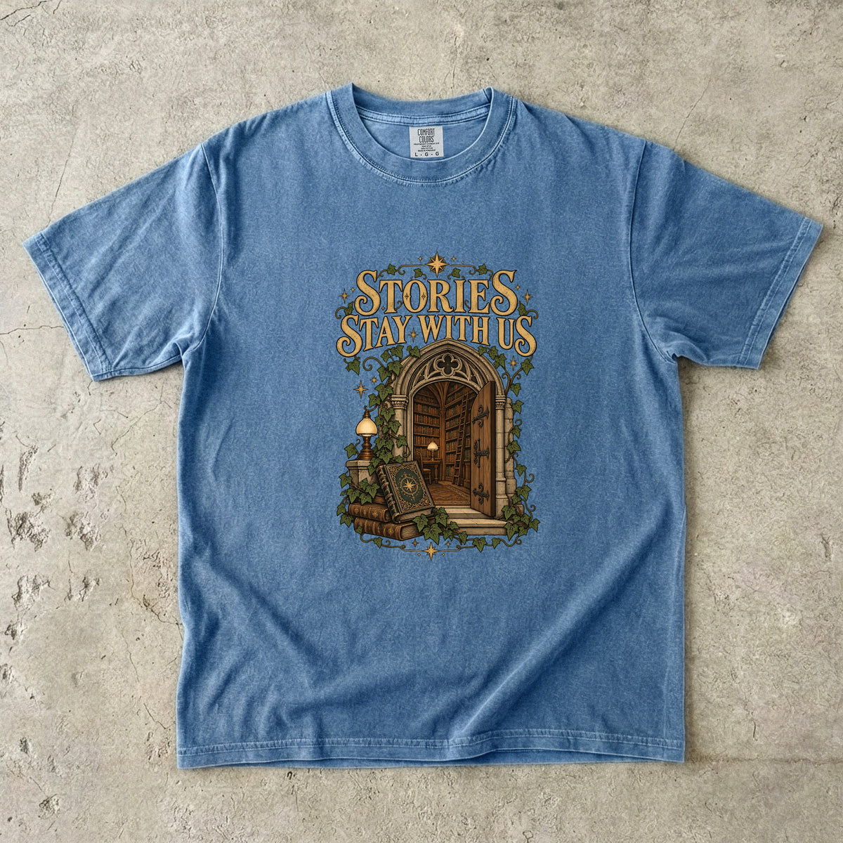 Blue Jean T-shirt featuring “Stories Stay With Us” with an ivy-covered arched library doorway, antique books, lamps and gold stars.