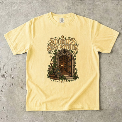 Butter T-shirt featuring “Stories Stay With Us” with an ivy-covered arched library doorway, antique books, lamps and gold stars.