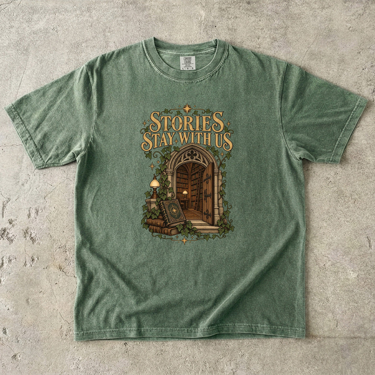 Moss T-shirt featuring “Stories Stay With Us” with an ivy-covered arched library doorway, antique books, lamps and gold stars.