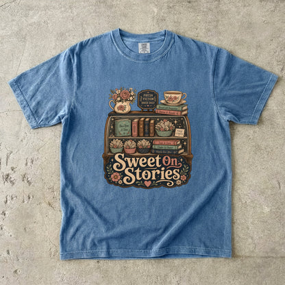 Sweet on Stories book lover T-shirt in Blue Jean featuring a vintage fresh-fiction display with books, page cakes, flowers and teacup
