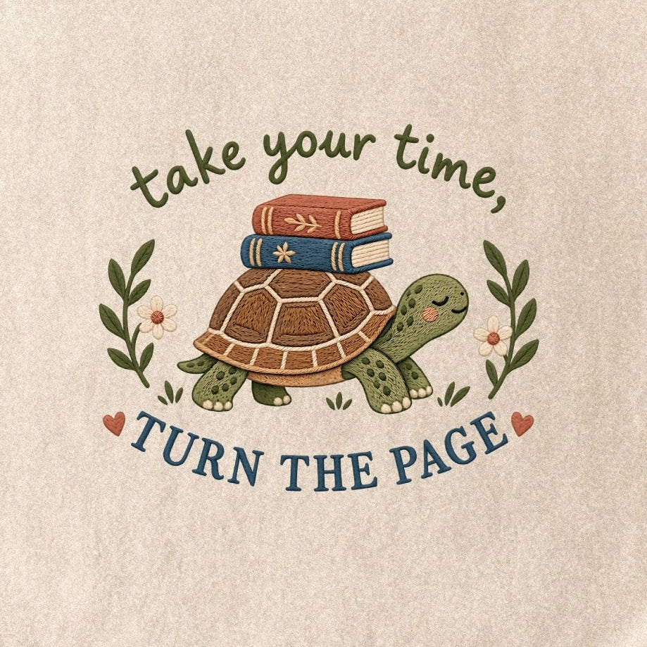 Close-up of the “take your time, TURN THE PAGE” T-shirt design, showing a smiling turtle carrying two books, leafy sprigs, daisies and small hearts.