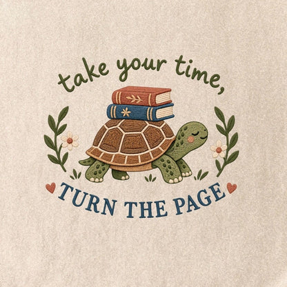 Close-up of the “take your time, TURN THE PAGE” T-shirt design, showing a smiling turtle carrying two books, leafy sprigs, daisies and small hearts.