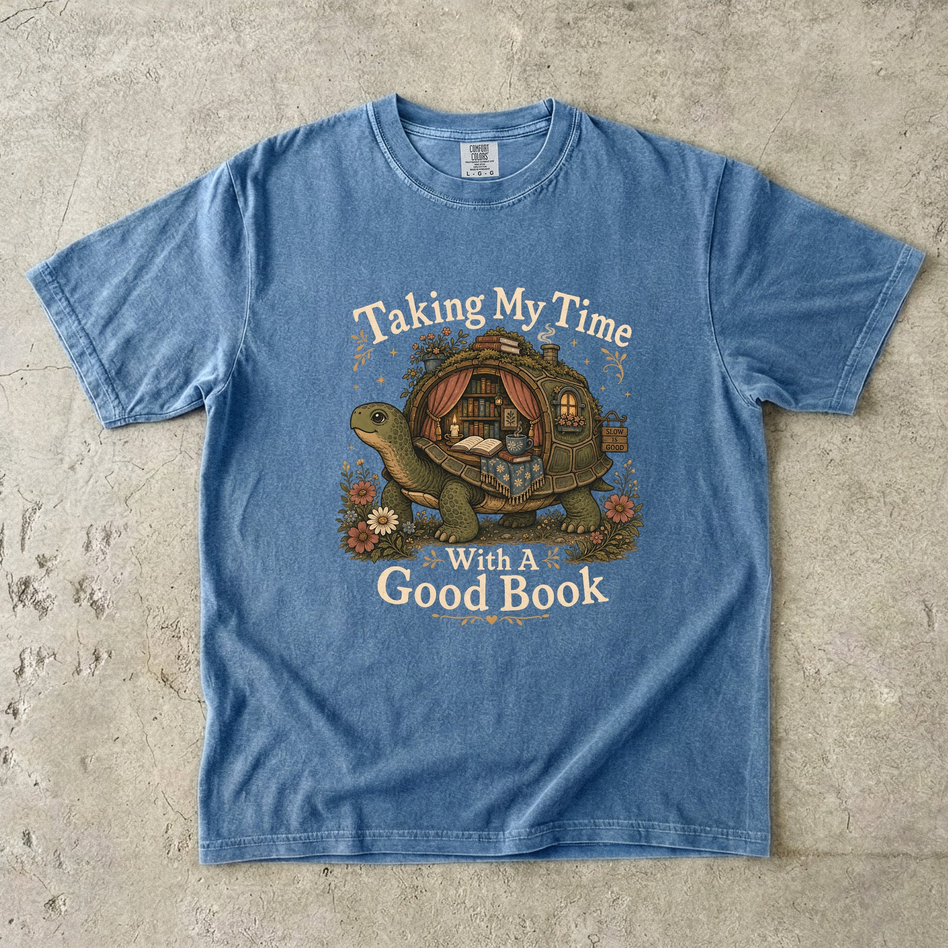 Taking My Time With a Good Book T-shirt in Blue Jean featuring a tortoise carrying a cozy book-filled reading retreat