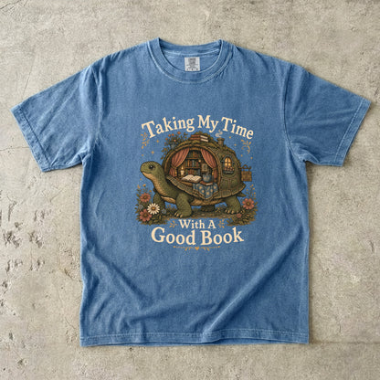 Taking My Time With a Good Book T-shirt in Blue Jean featuring a tortoise carrying a cozy book-filled reading retreat