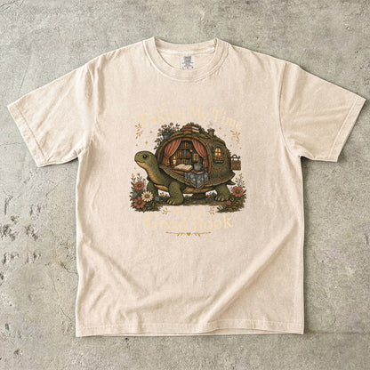 Taking My Time With a Good Book T-shirt in Ivory featuring a tortoise carrying a cozy book-filled reading retreat