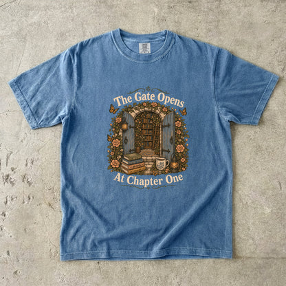 The Gate Opens at Chapter One literary T-shirt in Blue Jean featuring open gates leading into a flower-filled hidden library