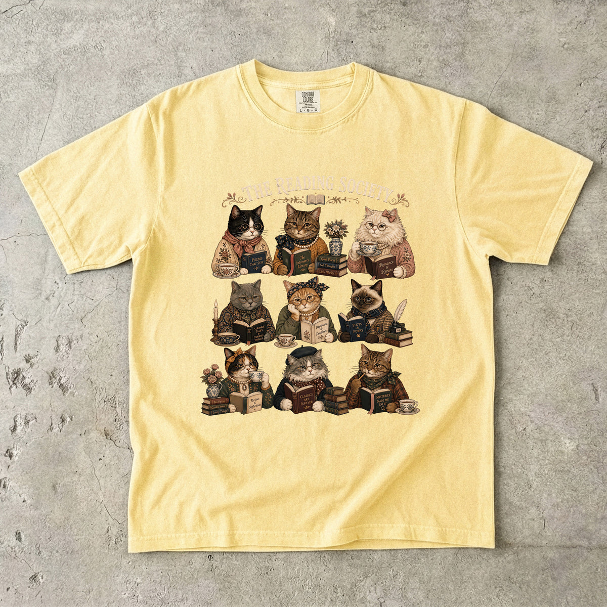 The Reading Society cat book club T-shirt in Butter featuring nine cats reading books with teacups and vintage accessories
