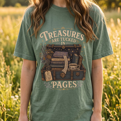 Lifestyle image of a model wearing the Comfort Colors 1717 T-shirt in Seafoam featuring the "Treasures Are Tucked in Pages" vintage illustration with an open treasure chest, books, flowers and a teacup in a wildflower meadow. 