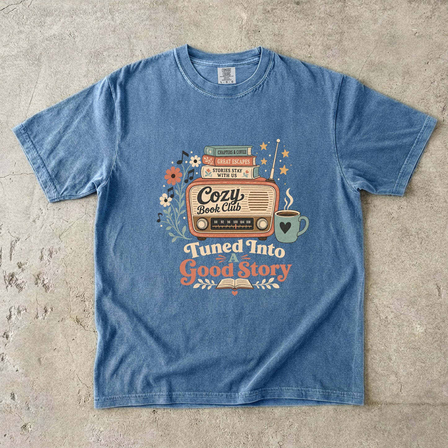 Front view of a Blue Jean Comfort Colors Book Lover T-shirt featuring the Tuned Into a Good Story retro literary design.