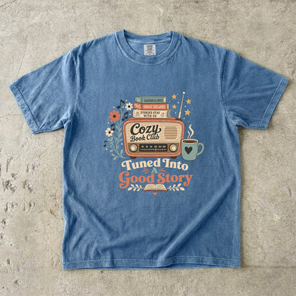 Front view of a Blue Jean Comfort Colors Book Lover T-shirt featuring the Tuned Into a Good Story retro literary design.