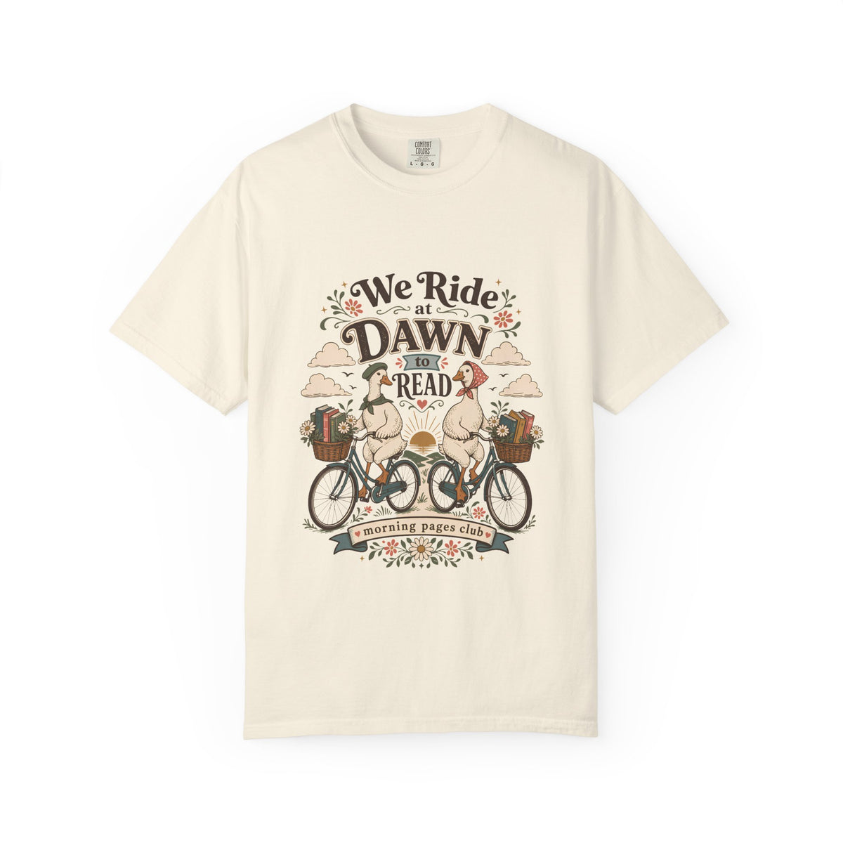 We Ride at Dawn to Read book lover T-shirt featuring two geese riding bicycles with baskets of books and flowers on Ivory.