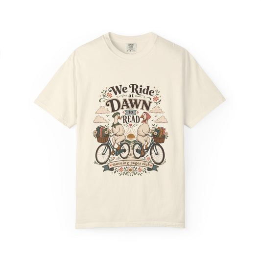 We Ride at Dawn to Read book lover T-shirt featuring two geese riding bicycles with baskets of books and flowers on Ivory.